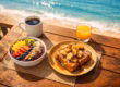 Acai bowl with fresh fruits and bananas foster French toast on a wooden table overlooking the ocean in Lauderdale-by-the-Sea